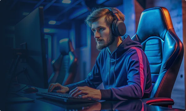 Un joueur concentré, assis à un bureau dans une pièce faiblement éclairée, coiffé d'un sweat à capuche et équipé d'un casque, tape sur son clavier. La scène est baignée d'une lumière bleue.